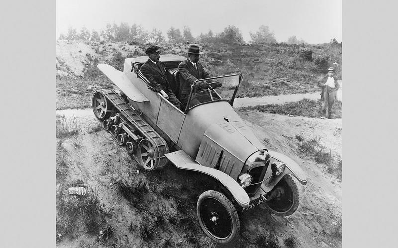 "Vintage Adolphe Kégresse half-track vehicle with rear rubber tracks and front wheels navigating rugged terrain."