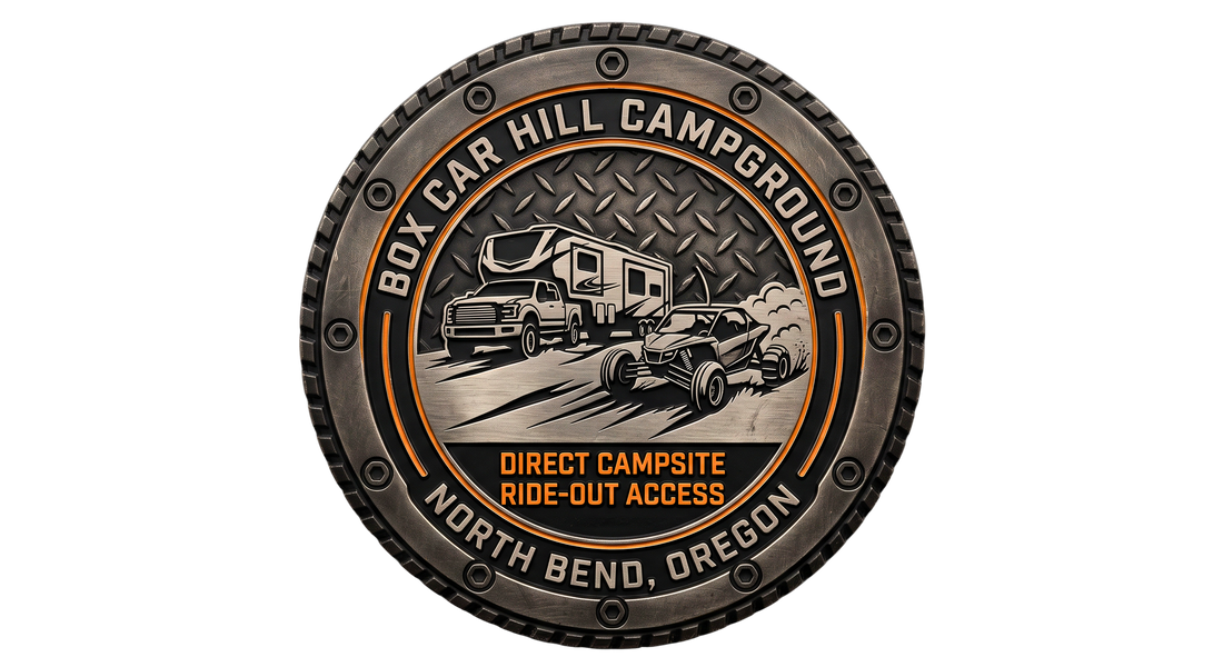 Close-up of a detailed challenge coin for Box Car Hill Campground in North Bend, Oregon. Centrally features an RV and UTV with sand spray, diamond plate texture, and "Direct Campsite Ride-Out Access