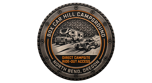 Close-up of a detailed challenge coin for Box Car Hill Campground in North Bend, Oregon. Centrally features an RV and UTV with sand spray, diamond plate texture, and "Direct Campsite Ride-Out Access