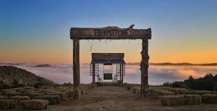 “Wooden archway labeled ‘Barnstone’ overlooking a valley filled with sunrise fog, with a wooden swing centered between posts and rows of hay bales in the foreground.”