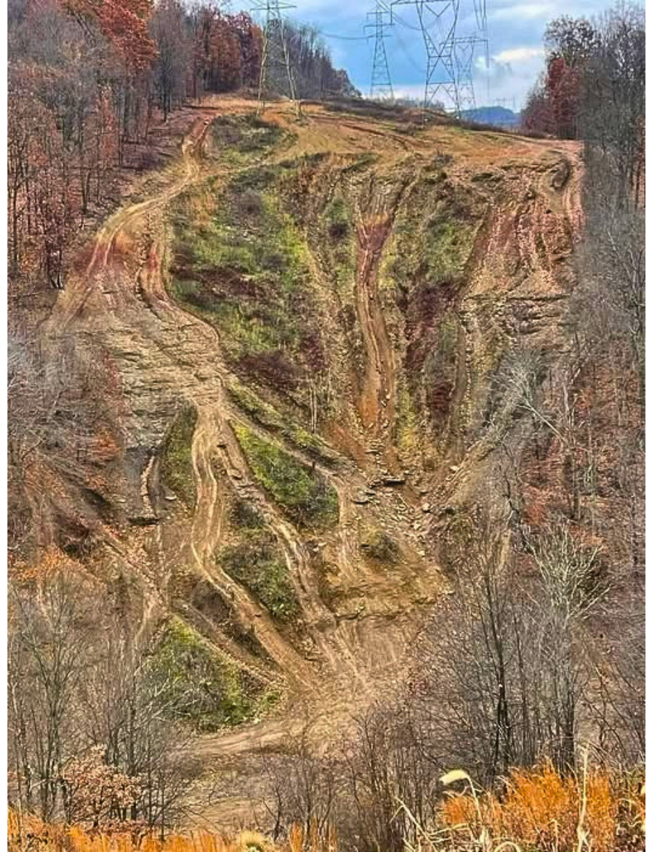 Steep eroded hill with deep ruts and exposed soil beneath powerline towers, surrounded by fall trees.